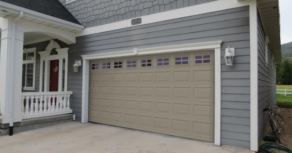 A beige sectional garage door on a grey house.